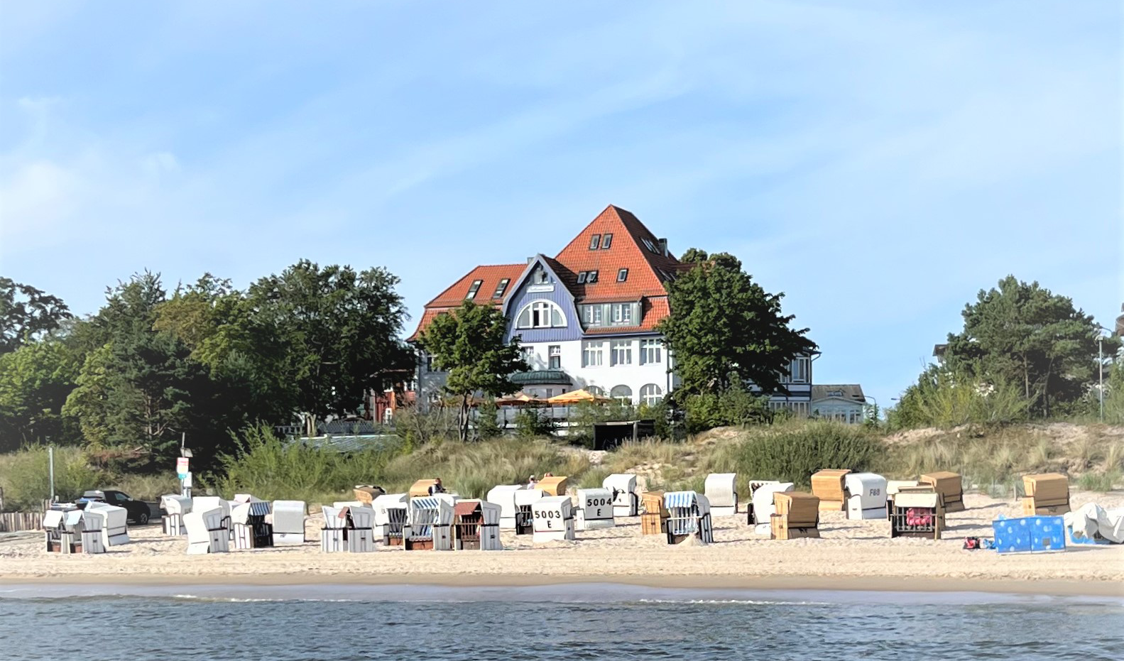 Verschiedene Strandkörbe auf Sand mit dem Hotel Strandvillen Heringsdorf im Hintergrund