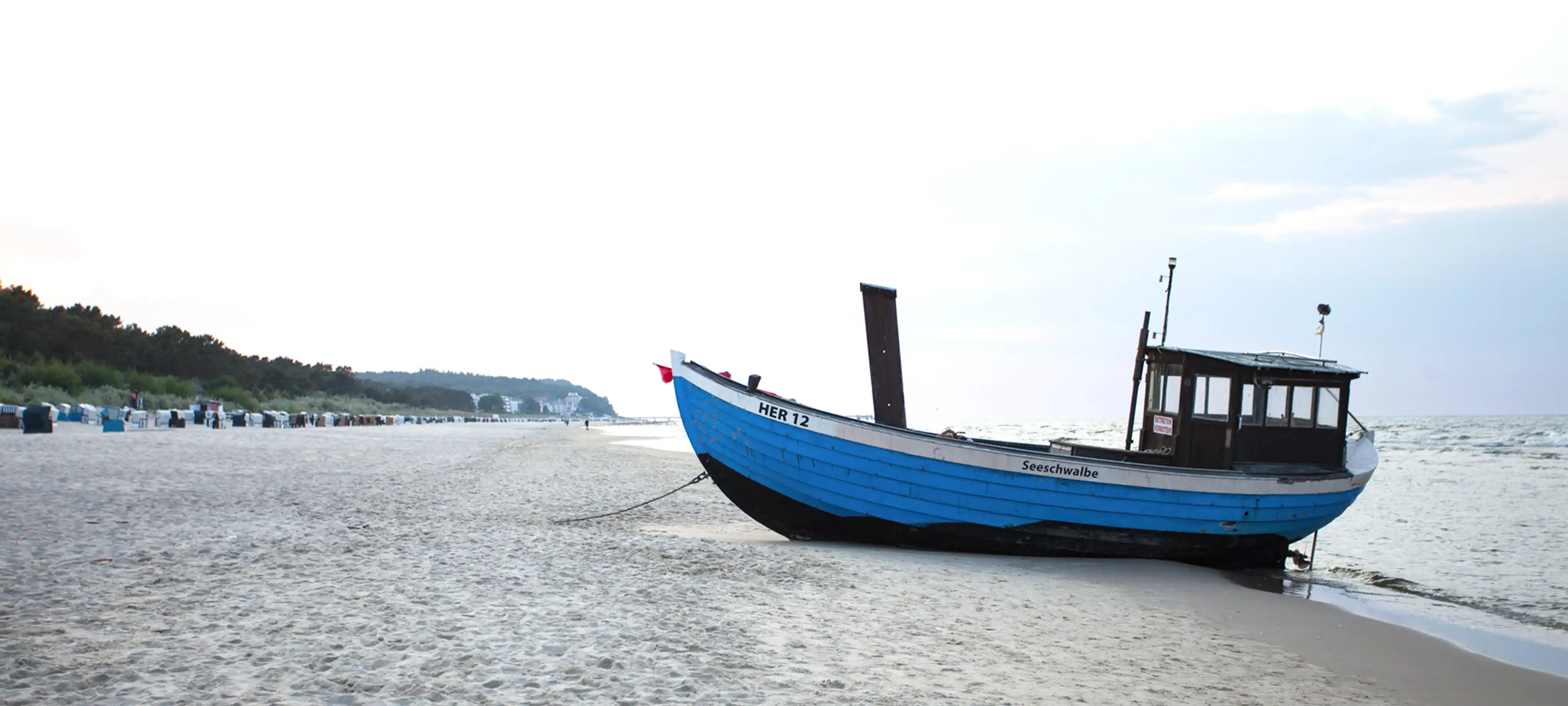 Verschiedene Strandkörbe auf Sand mit dem Hotel Strandvillen Heringsdorf im Hintergrund